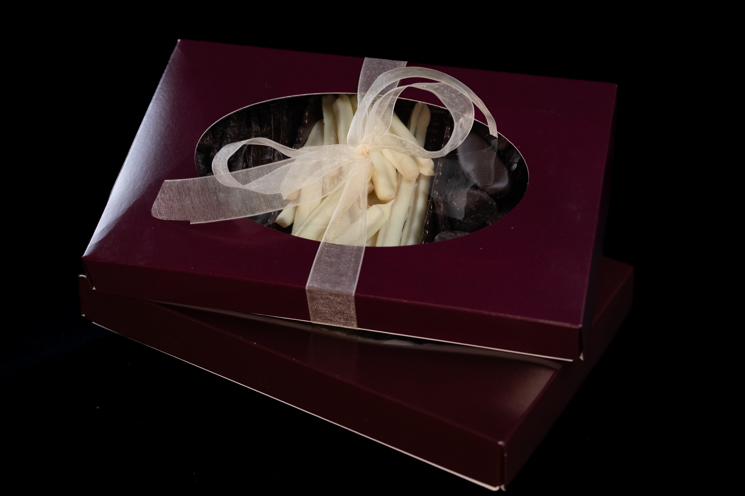 A box of candied and coated fruits, Chocolate Candied Orange Peels, White Chocolate Candied Lemon Peels, Dark Chocolate Candied Ginger, with a transparent window revealing the contents, tied with a ribbon.