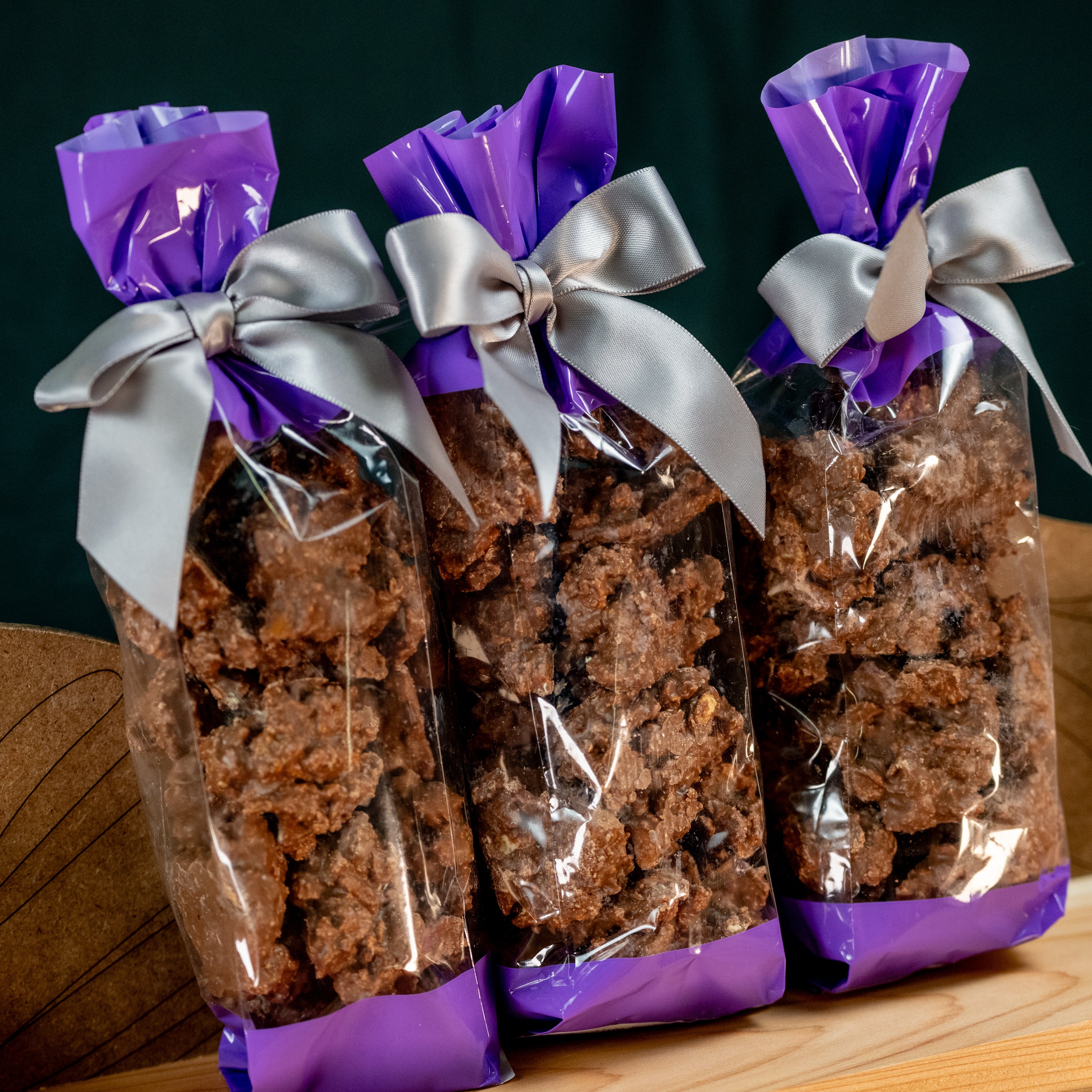 Three gift bags of Milk Chocolate Pretzel Poppers tied with silver ribbons and purple wrap, perfect for gifting or snacking.