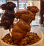Chocolate bunny lollipops on sticks — dark and milk chocolate variants with hand-painted red ears — displayed in a bowl of coffee beans by the shop window.
