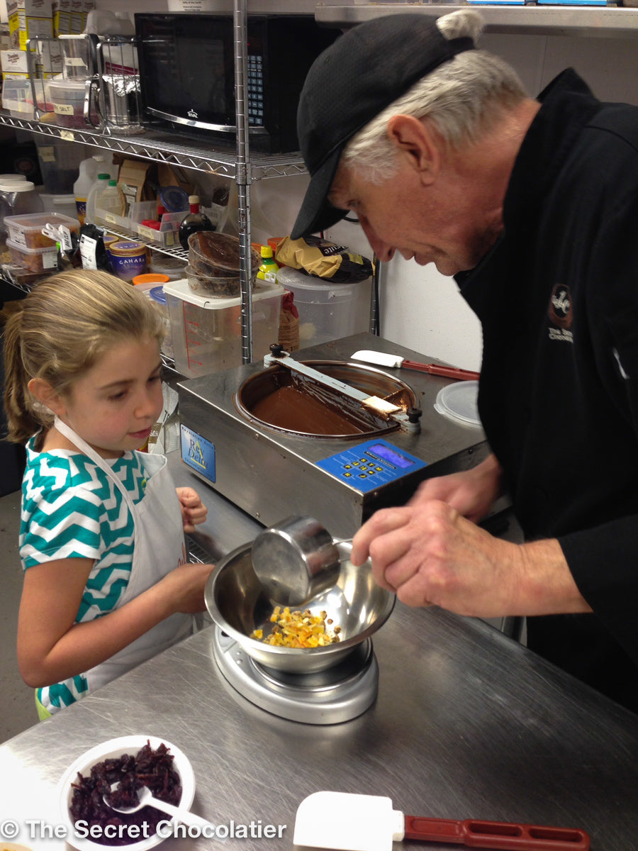 Chef guiding a young participant through chocolate bark preparation during a hands-on workshop at The Secret Chocolatier, offering a fun and educational chocolate-making experience for kids in Charlotte, NC.