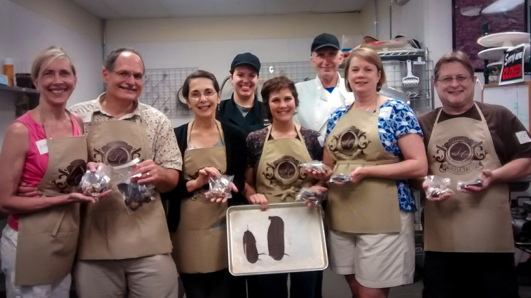 Group of participants at The Secret Chocolatier’s chocolate tempering workshop in Charlotte, NC, proudly holding finished chocolates and a temper test sheet.