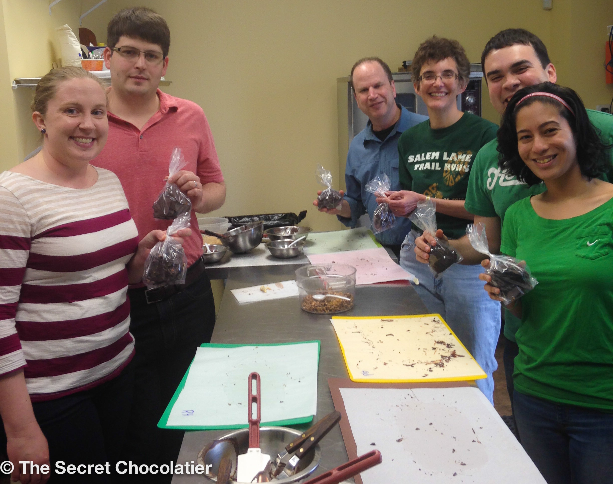 Group of smiling participants holding chocolate bags at a hands-on chocolate tempering workshop at The Secret Chocolatier.