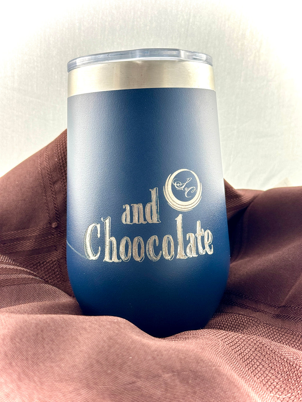 Navy stainless steel tumbler etched with 'and Chocolate' beneath The Secret Chocolatier monogram, displayed on a mauve drape.