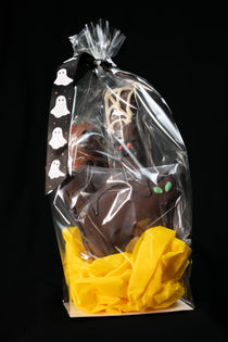 Halloween Treat Bag — clear cellophane tied with a black-and-white ghost-pattern ribbon, holding chocolate Halloween shapes on yellow tissue.