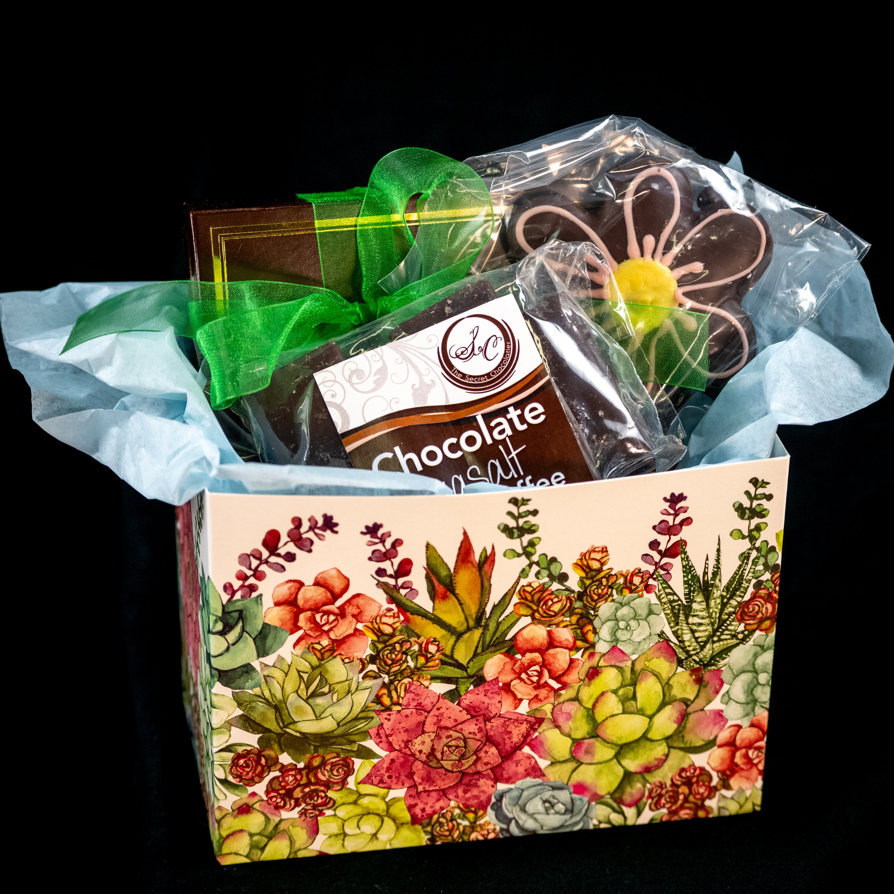 Mother's Day chocolate gift box — succulent-illustrated kraft box with green ribbon containing Chocolate Sea Salt Butter Toffee and a chocolate daisy-shaped cookie. Main image