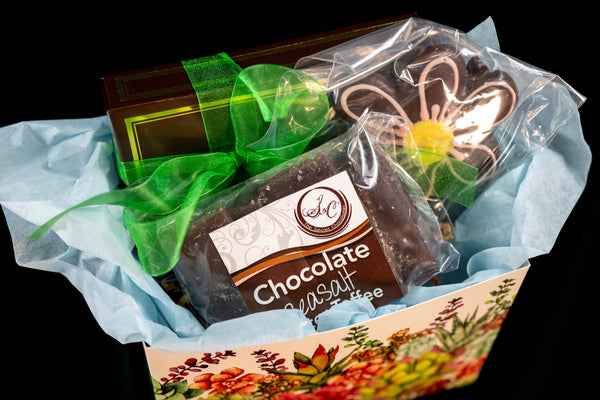 Mother's Day gift box detail — Chocolate Sea Salt Butter Toffee, a chocolate daisy cookie, and TSC chocolates wrapped with a green ribbon in a floral-pattern box.