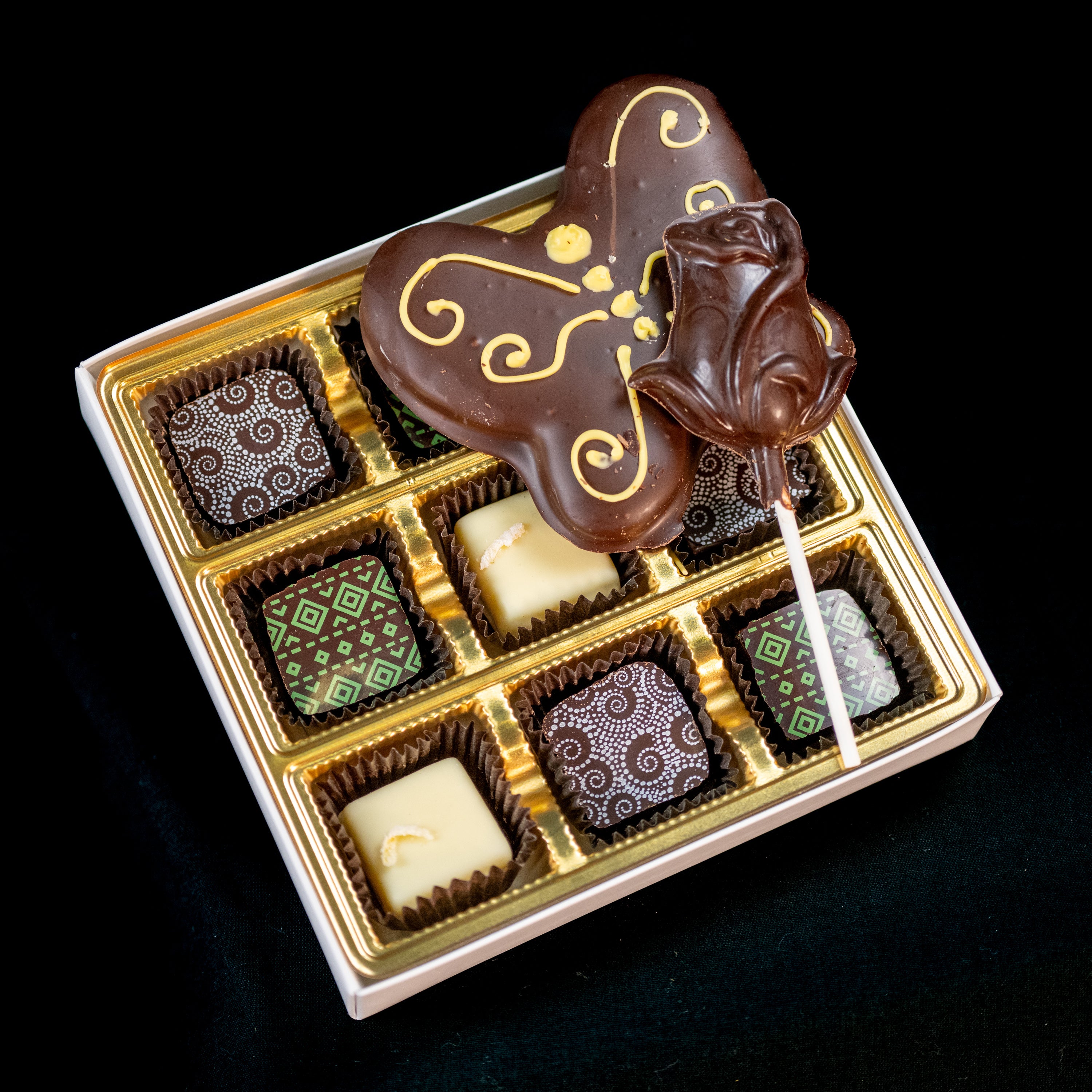 Mother's Day chocolate assortment — ornate gift box with a gold-filigree chocolate butterfly, a chocolate rose pop, and six patterned bonbons.