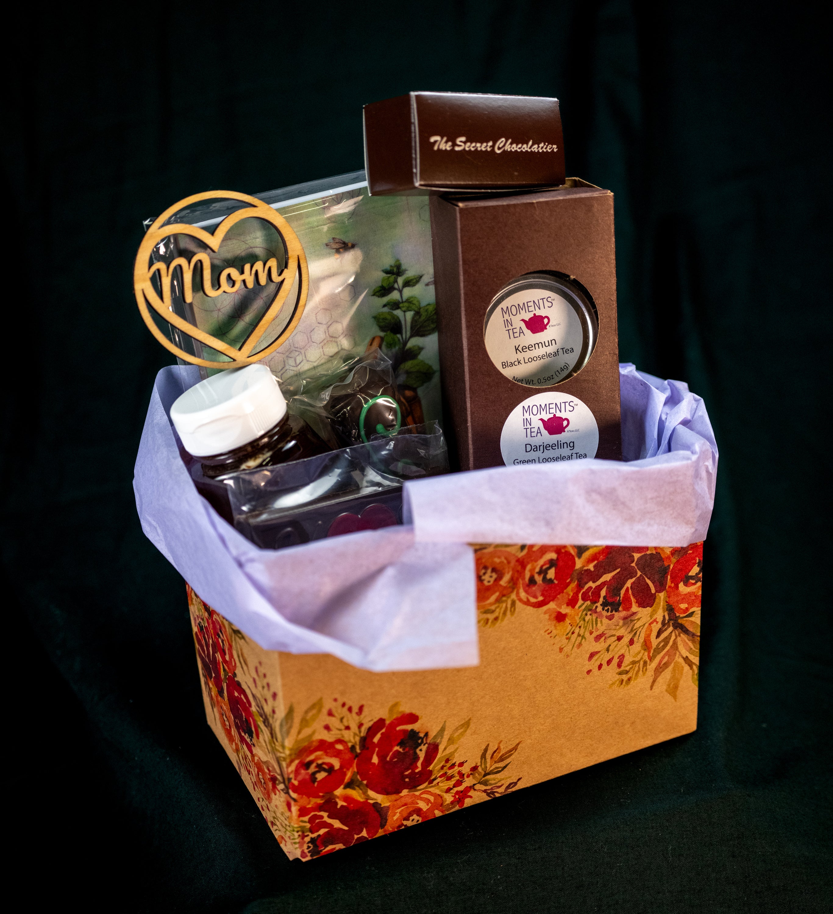 Mother's Day Tea & Chocolate gift box — Moments In Tea Keemun Black and Darjeeling Green tea tins, TSC chocolates, and a wooden 'Mom' heart ornament in a floral-print box.