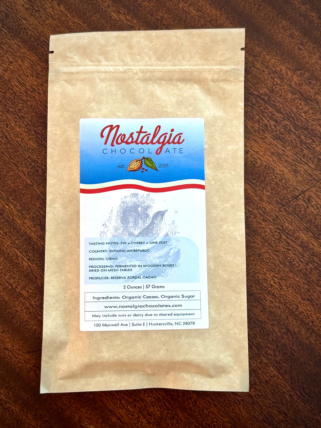 Nostalgia Chocolate Dominican Republic single-origin bar in a kraft-paper bag with a light-blue cacao-pod label — Reserva Zorzal cacao, fig, cherry, and lime zest tasting notes.