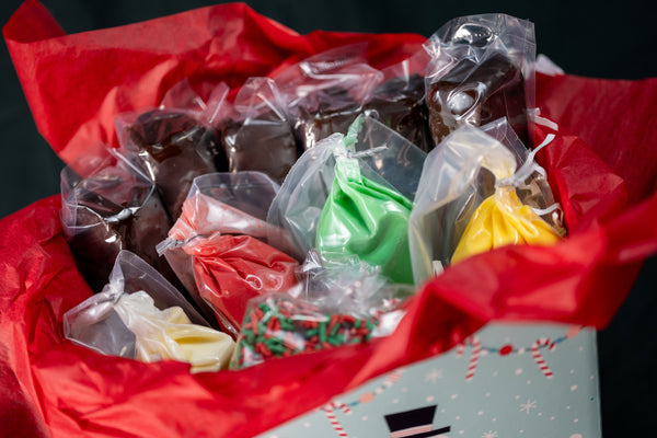 Brownie Pop Decorating Kit Christmas variant — open box showing brownie pops, red/green/yellow icing piping bags, and red/green sprinkles.