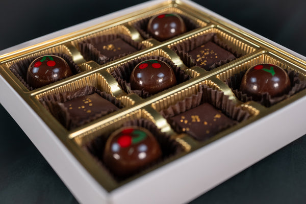 Dairy-Free Decadence sampler at an angle — Candied Cherry Coconut Milk Caramel bon bons with hand-painted cherry motifs alongside square dark chocolate truffles finished in gold sprinkles.