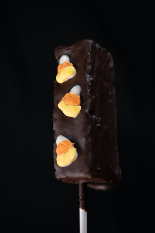 Brownie Pop — chocolate-coated brownie on a stick with yellow, orange, and white icing accents along the side.