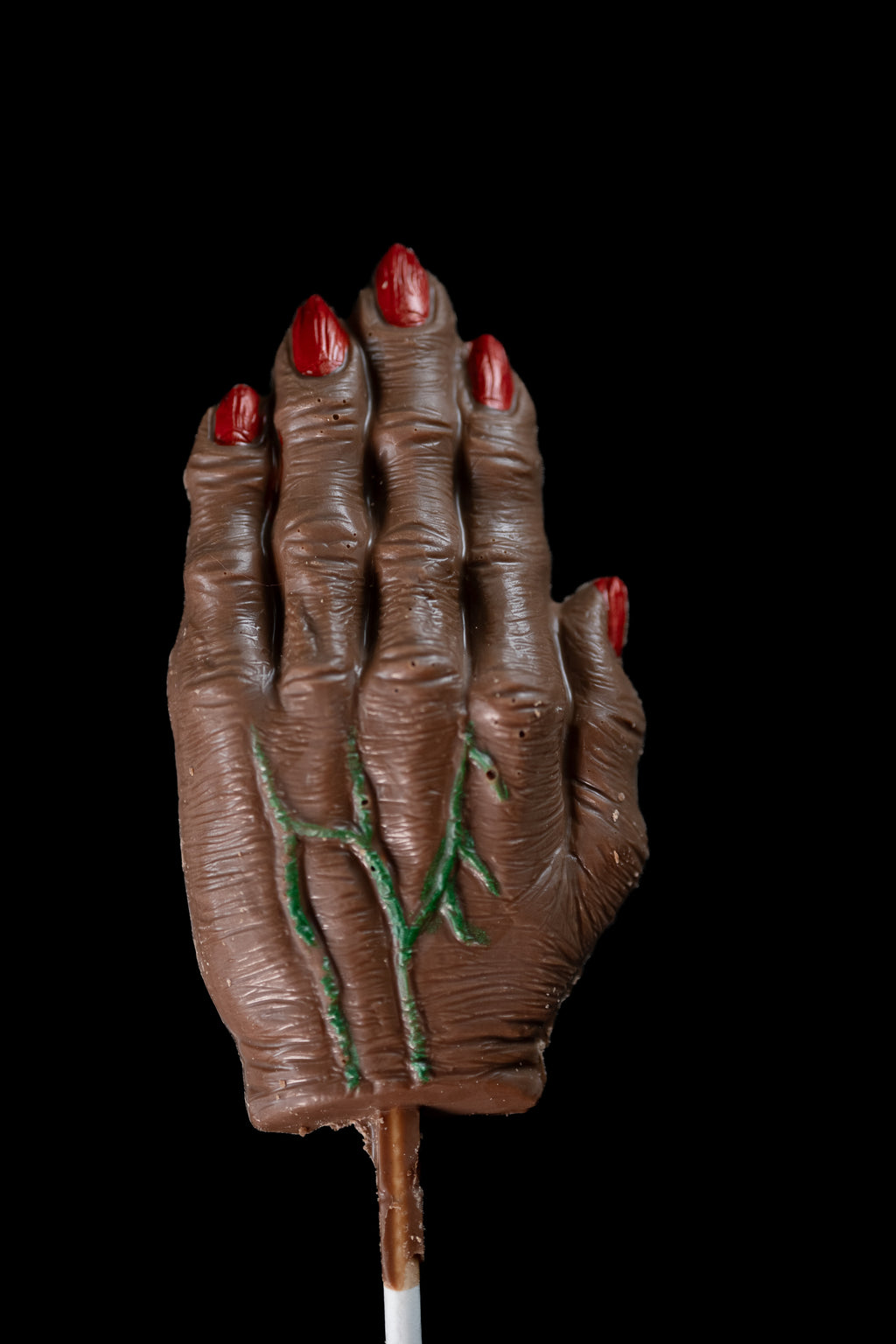 Milk chocolate witch hand lollipop with red-painted fingernails and green-piped veins across the knuckles.