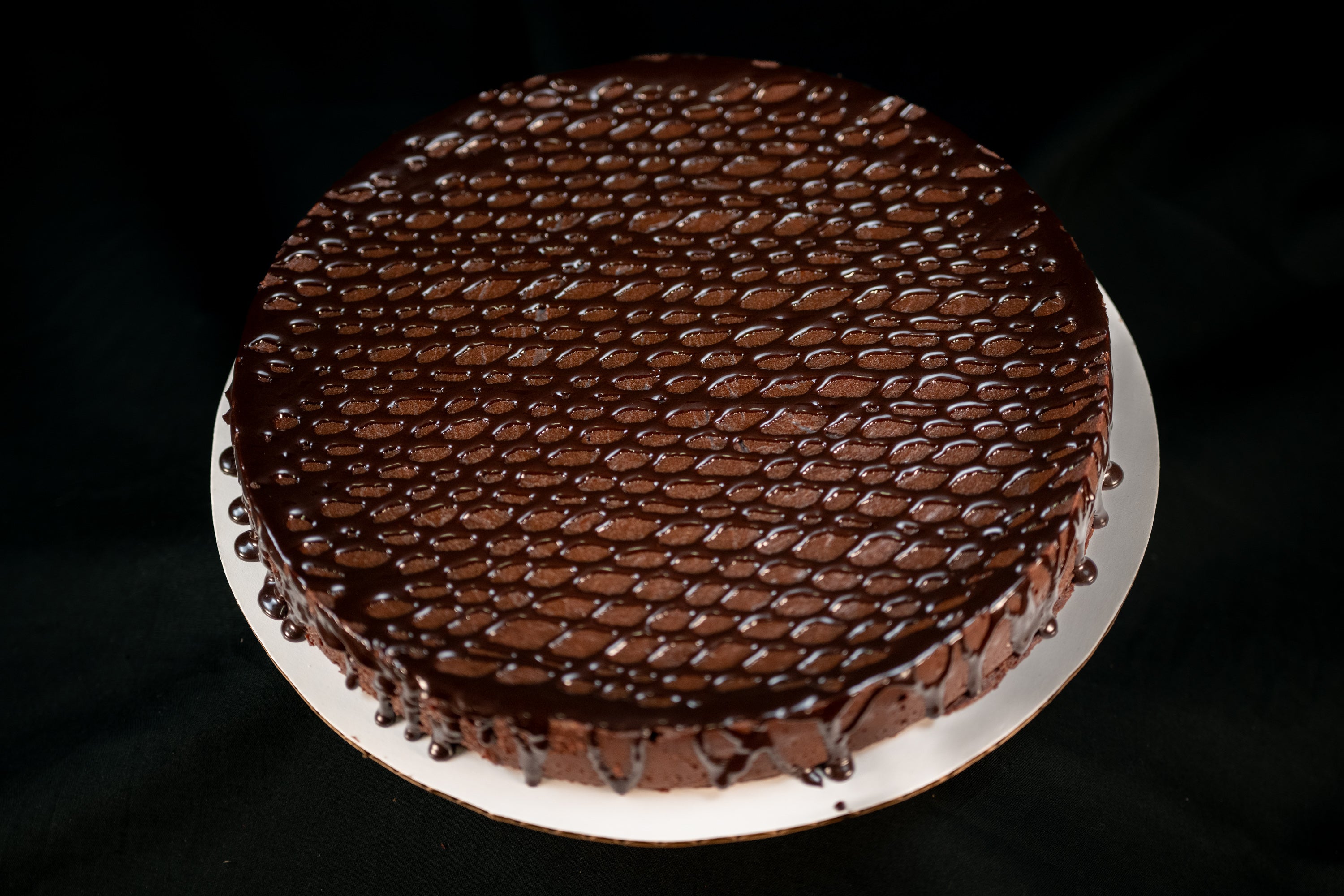 Round Chocolate Oblivion Torte with a glossy quenelle-patterned ganache top and dripping edges, on a white board. Main image