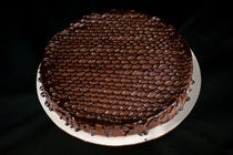 Round Chocolate Oblivion Torte with a glossy quenelle-patterned ganache top and dripping edges, on a white board.
