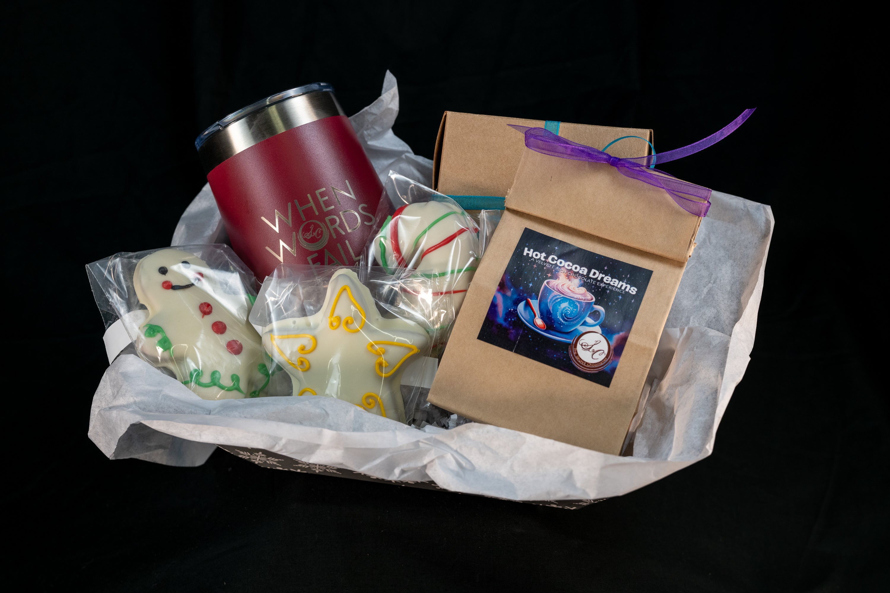 The Cozy Cocoa Collection gift basket — pink Secret Chocolatier tumbler, Hot Cocoa Dreams pouch, peppermint truffle ball, and hand-piped snowman and angel chocolates.
