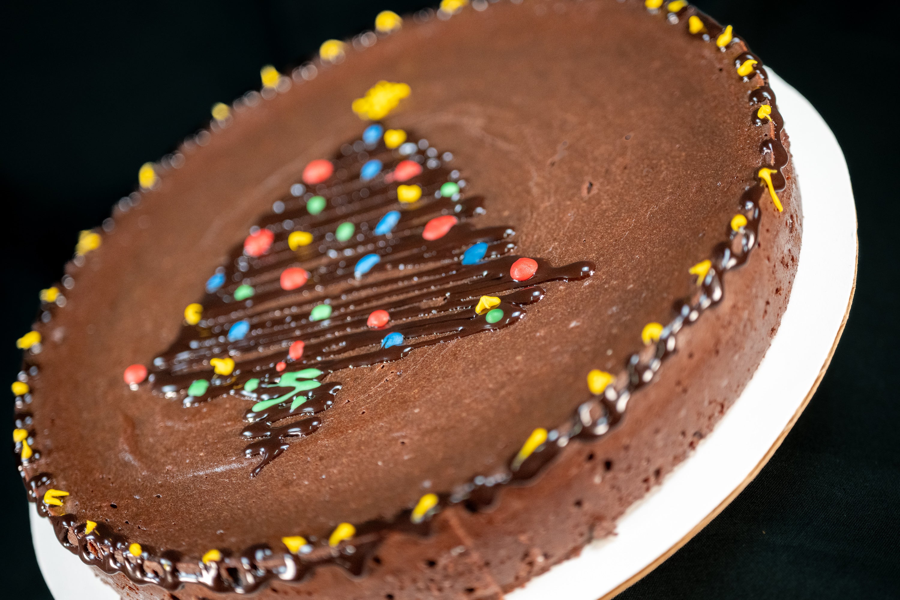Chocolate Oblivion Torte decorated for the holidays — hand-piped Christmas tree in chocolate with red, green, blue, and yellow ornament dots and yellow rim accents.