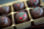 Candied Cherry & Coconut Milk Bon Bons in a gift box, each round chocolate dome painted with a red cherry and green stem motif.