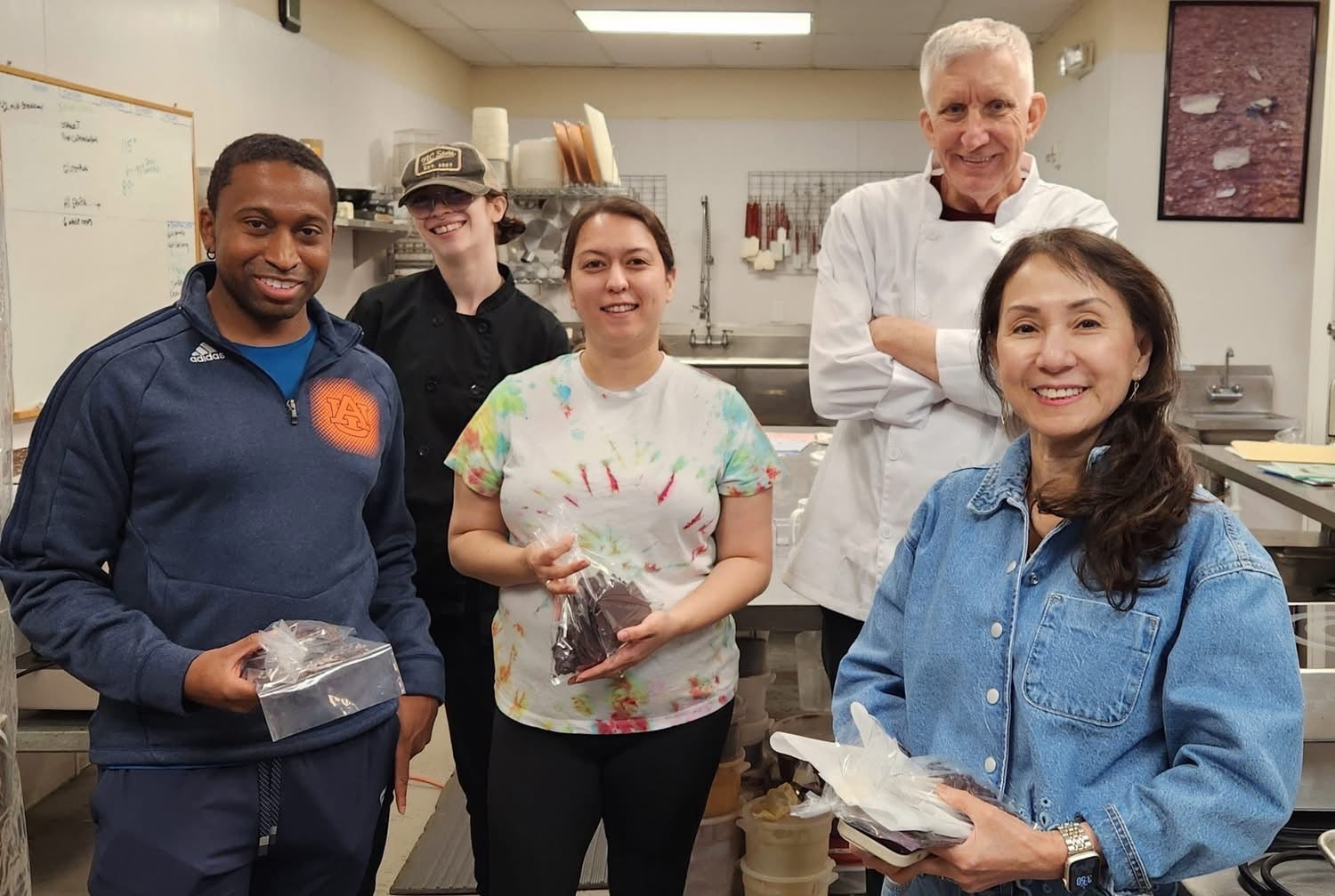 Smiling participants holding finished chocolate bark during a hands-on class at The Secret Chocolatier, showcasing their homemade creations in the chocolate kitchen. Main image