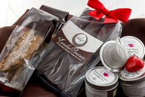 Tea & Chocolate Indulgence Kit components — TSC Enrobed Brownies and biscotti, three Moments In Tea tins, and a mesh tea strainer with a red heart charm.