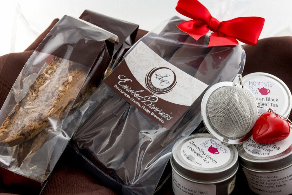 Tea & Chocolate Indulgence Kit components — TSC Enrobed Brownies and biscotti, three Moments In Tea tins, and a mesh tea strainer with a red heart charm.