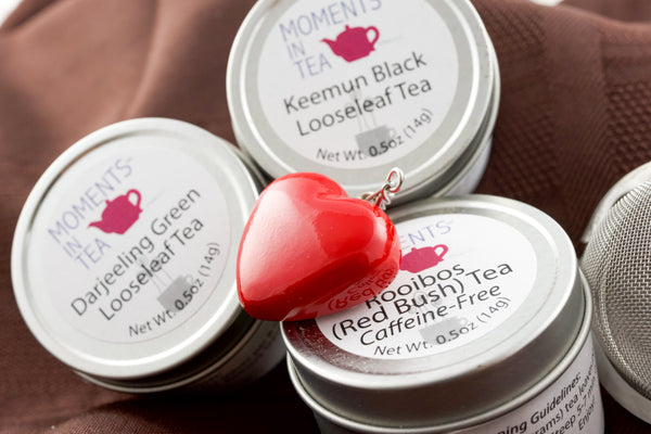 Three Moments In Tea tins (Keemun Black, Darjeeling Green, Rooibos Red Bush Caffeine-Free) with a red heart-shaped tea strainer.