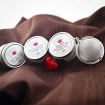 Moments In Tea tins (Keemun Black, Darjeeling Green, Rooibos Red Bush) lined up with a red heart-shaped tea strainer.