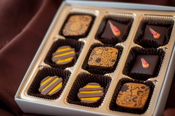 Adventurous Chocolate 9-piece box — bonbons with hand-painted decorative patterns in gold and red, featuring bold exotic flavors.