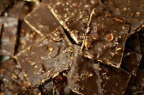 Pile of Dark Chocolate Toasted Almond Bark squares with chopped toasted almonds embedded throughout the dark chocolate.