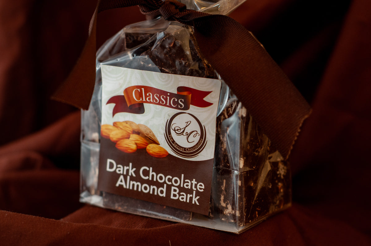 Close stack of Dark Chocolate Toasted Almond Bark pieces showing chopped almonds across the chocolate surface.