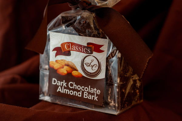 Close stack of Dark Chocolate Toasted Almond Bark pieces showing chopped almonds across the chocolate surface.