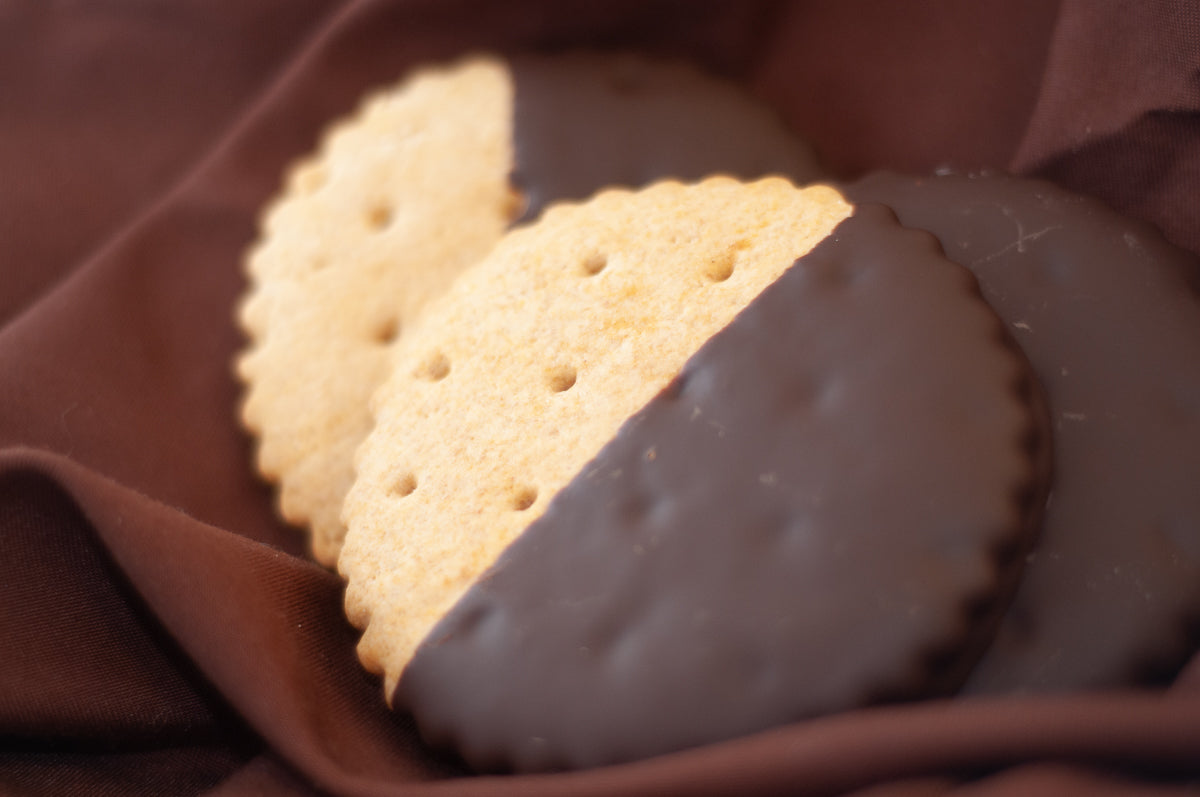 Round graham crackers half-dipped in dark chocolate, displayed on brown fabric. Main image