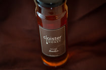 Cloister Honey Infused Bourbon Honey bottle with a brown label, on burgundy fabric.