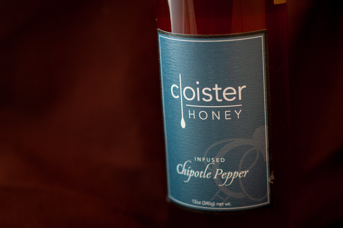 Cloister Honey Infused Chipotle Pepper Honey bottle with a teal label, on burgundy fabric.