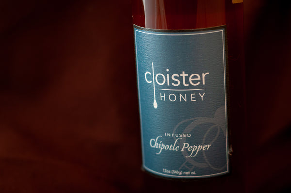 Cloister Honey Infused Chipotle Pepper Honey bottle with a teal label, on burgundy fabric.