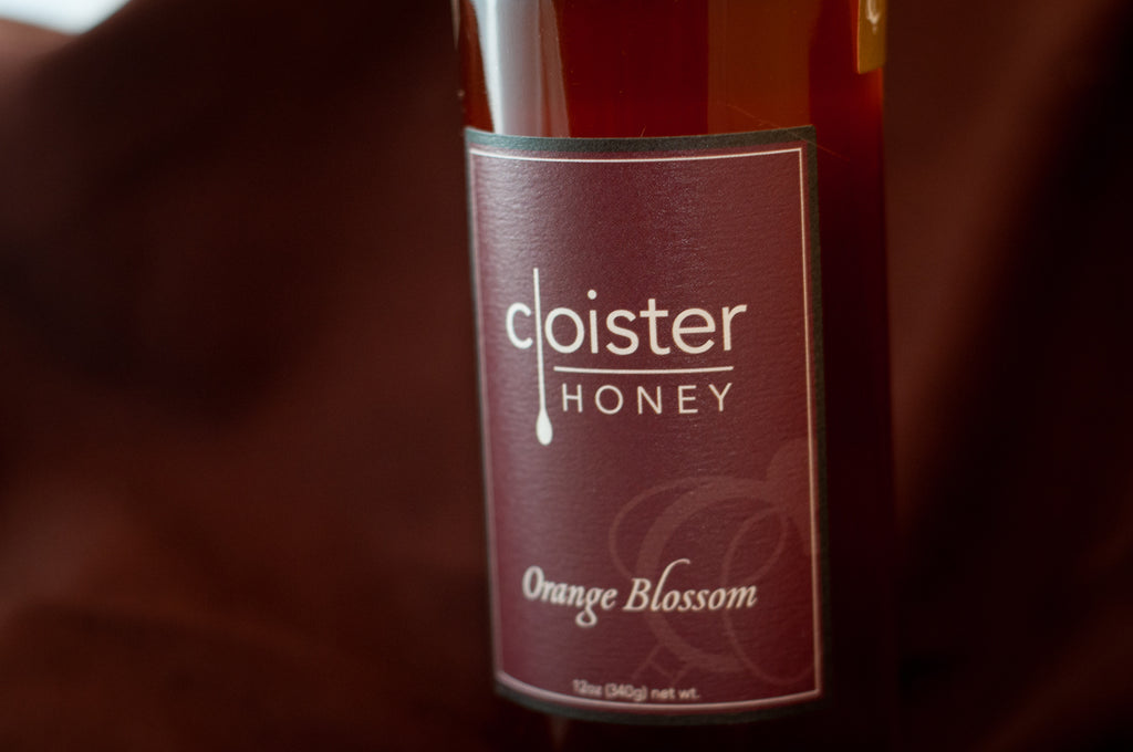 Cloister Honey Orange Blossom raw honey bottle with a deep maroon label, on burgundy fabric.
