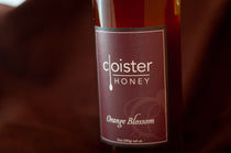 Cloister Honey Orange Blossom raw honey bottle with a deep maroon label, on burgundy fabric.