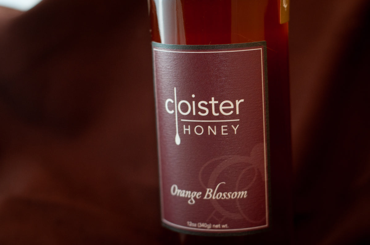Cloister Honey Orange Blossom raw honey bottle with a deep maroon label, on burgundy fabric.