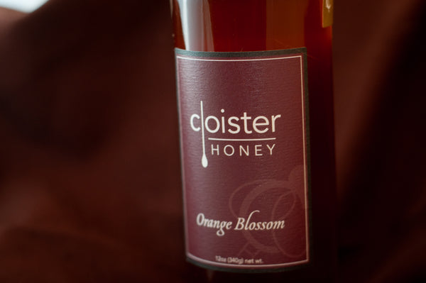 Cloister Honey Orange Blossom raw honey bottle with a deep maroon label, on burgundy fabric.