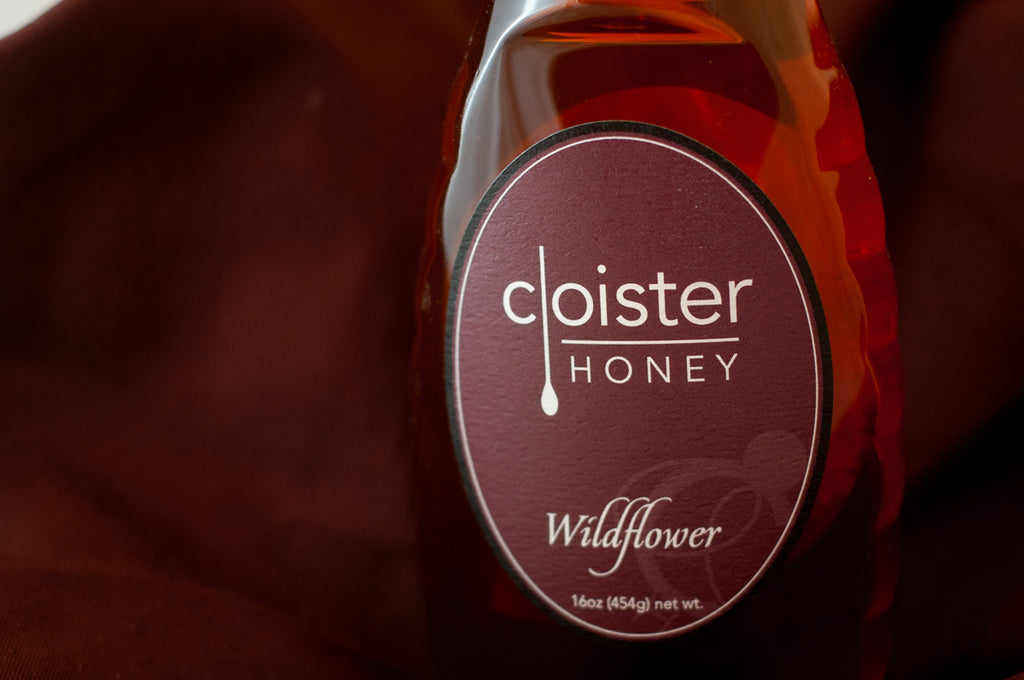 Cloister Honey Wildflower raw honey — 16 oz glass bottle with a maroon oval label, on burgundy fabric.