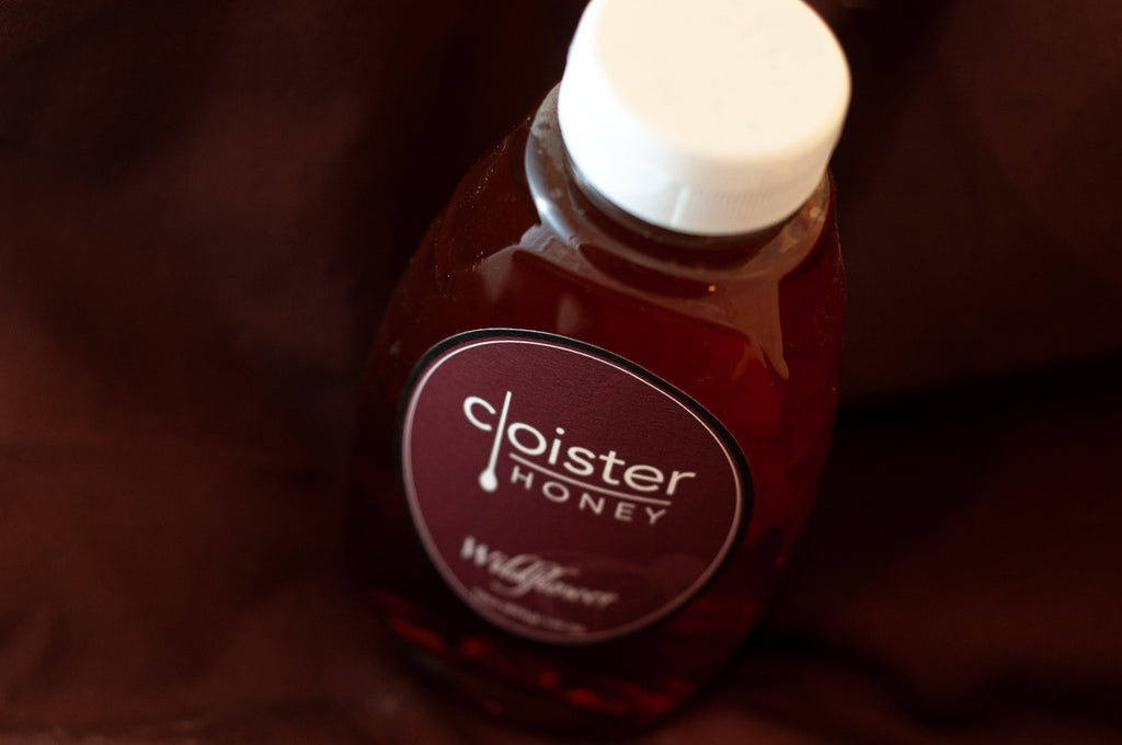 Cloister Honey Wildflower squeeze bottle with a white flip-cap and round maroon label, on burgundy fabric.