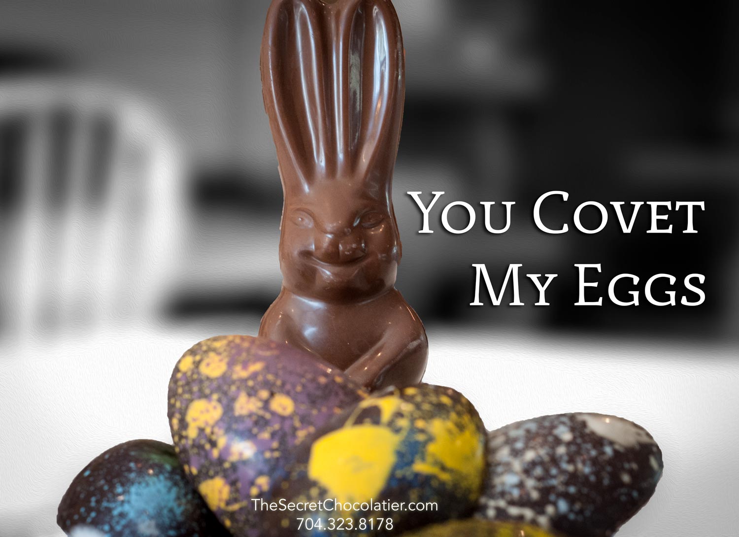 The Secret Chocolatier 'You Covet My Eggs' promotional graphic — a chocolate bunny standing in a pile of hand-painted speckled Easter eggs in purple, yellow, blue, and dark chocolate.