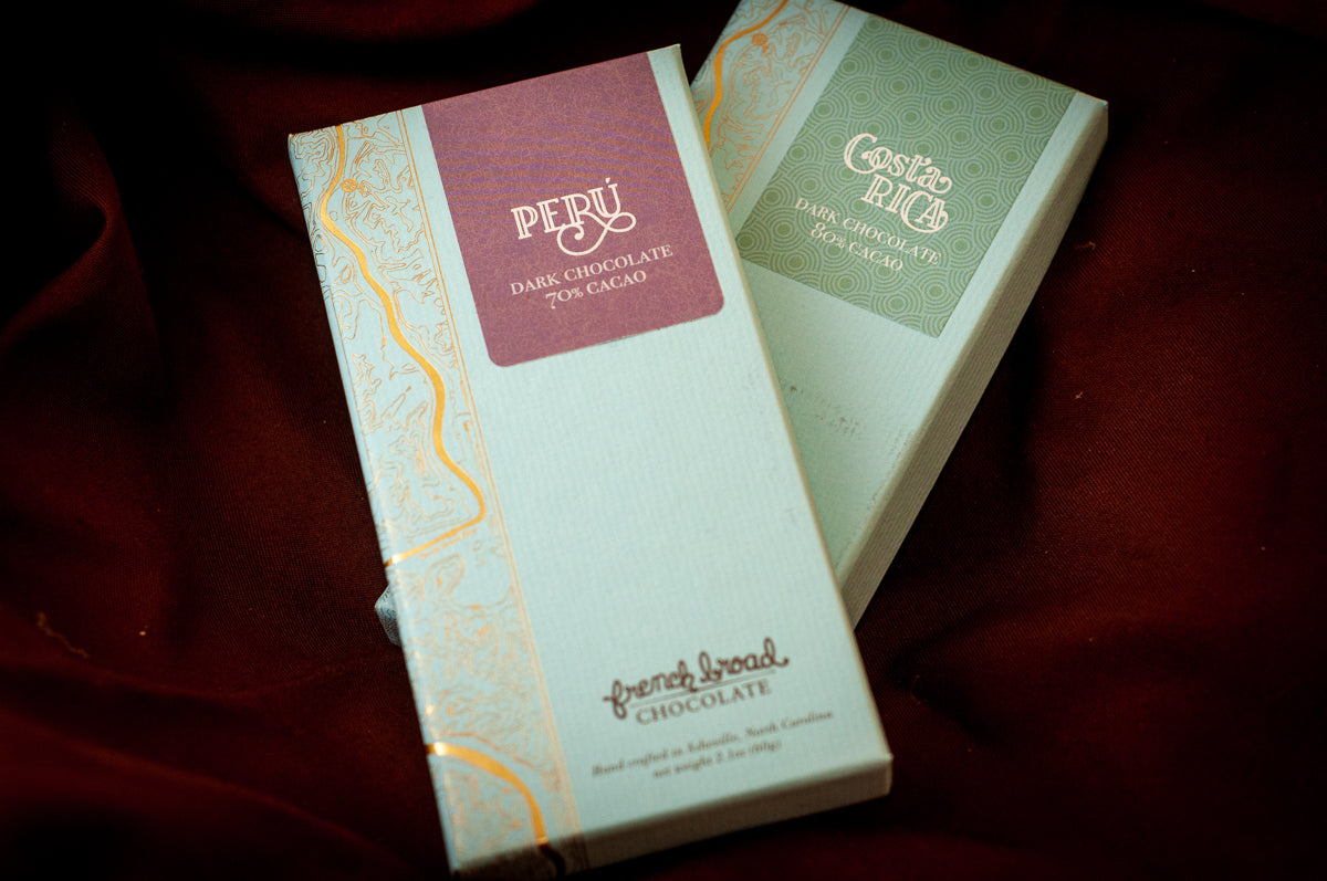 Two French Broad Chocolate single-origin bars — Peru 70% cacao and Costa Rica 80% cacao — in mint-blue and gold packaging on burgundy fabric. Main image