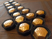 Cinnamon Roll Bon Bons arranged in dark paper candy cups, each with a piped chocolate-swirl top.