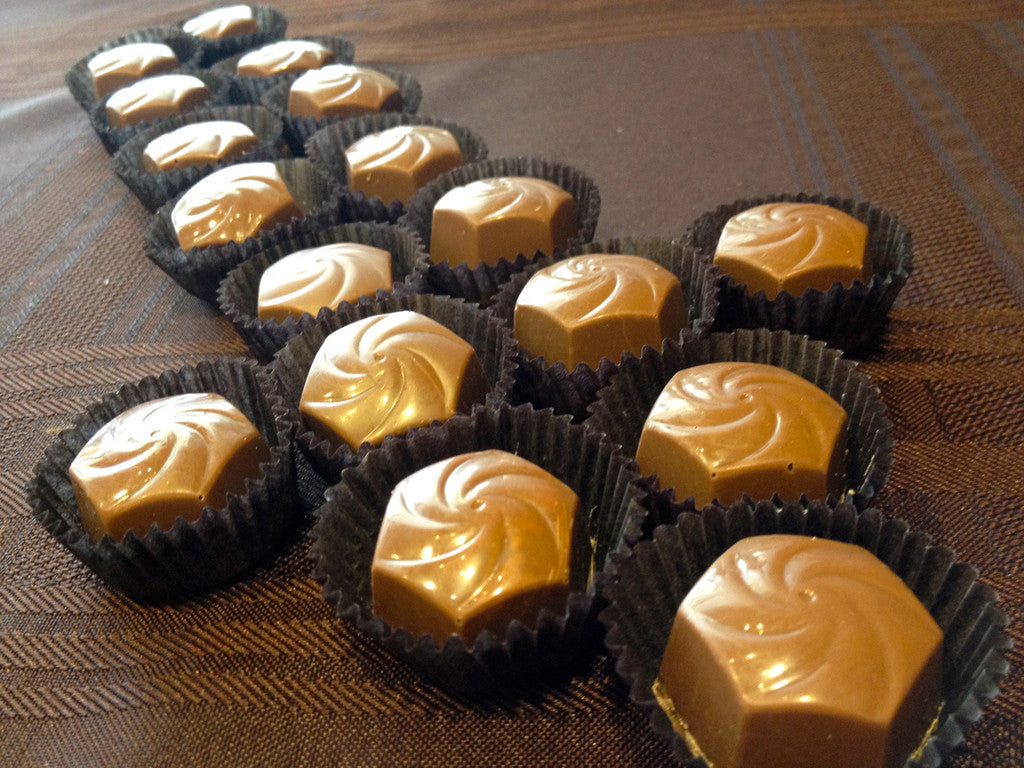 Cinnamon Roll Bon Bons arranged in dark paper candy cups, each with a piped chocolate-swirl top.