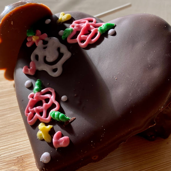 Valentine's chocolate-dipped heart treat hand-piped with pink and green flowers, yellow accents, a smiley face, and white pearl sprinkles.