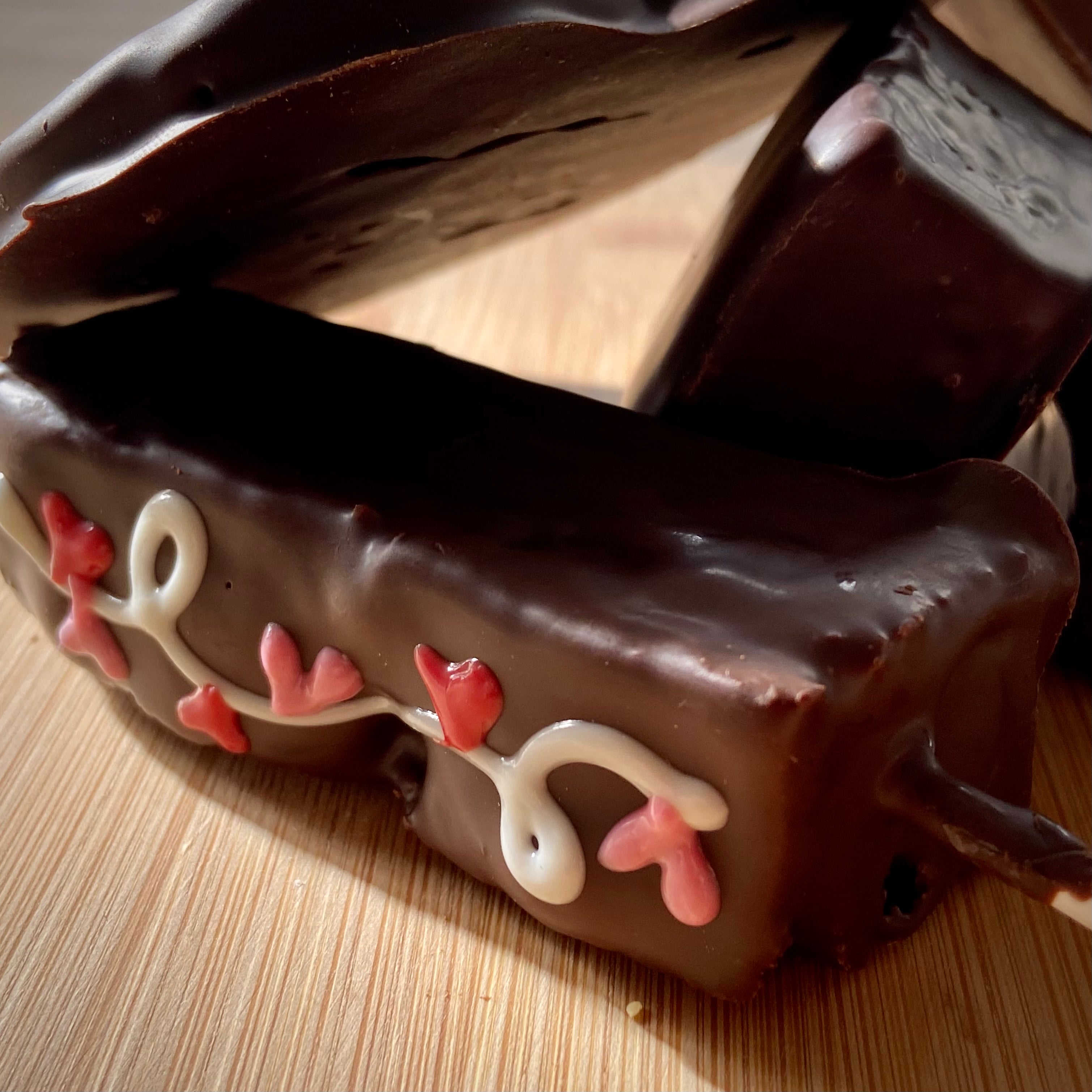 Chocolate-dipped Valentine's treat with white piped scrolls and pink heart accents, on a wooden surface.