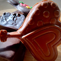 Valentine's milk chocolate heart lollipops molded with raised dot patterns and a plain heart, with a piped Valentine's heart treat in the background.