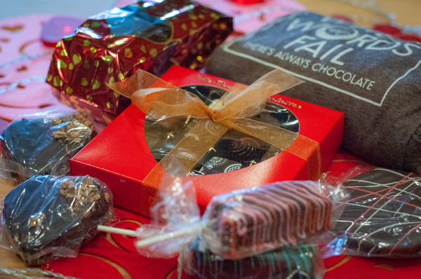 When Words Fail gift basket detail — red TSC truffle box with heart-shaped window, branded 'WORDS FAIL' shirt, and chocolate-covered pretzel pops.