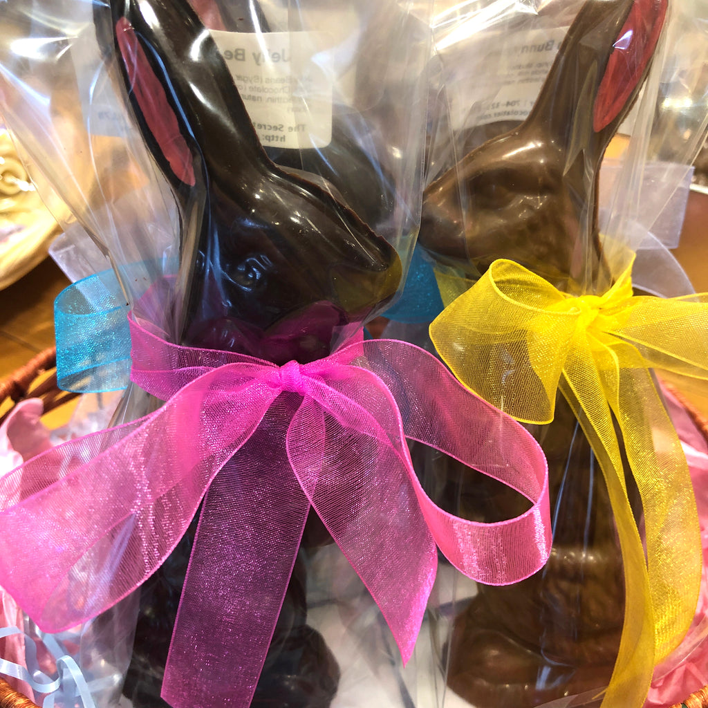 Two cellophane-wrapped chocolate Easter bunnies — dark chocolate with pink ribbon and milk chocolate with yellow ribbon — displayed on a counter.
